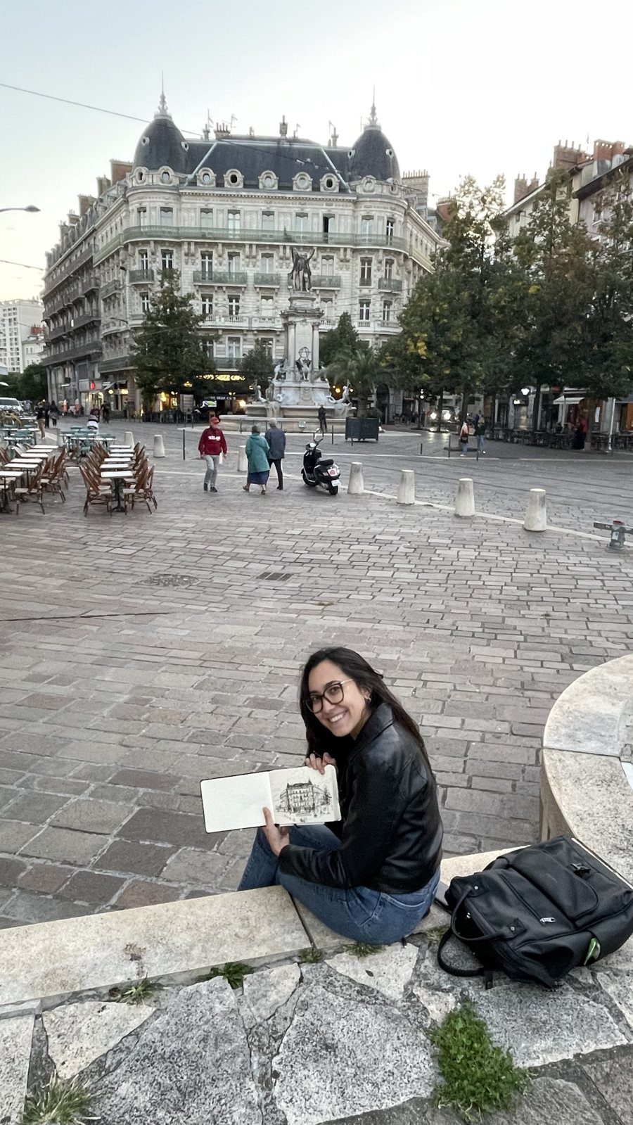 Aliya sitting on a city square, showing her sketchbook