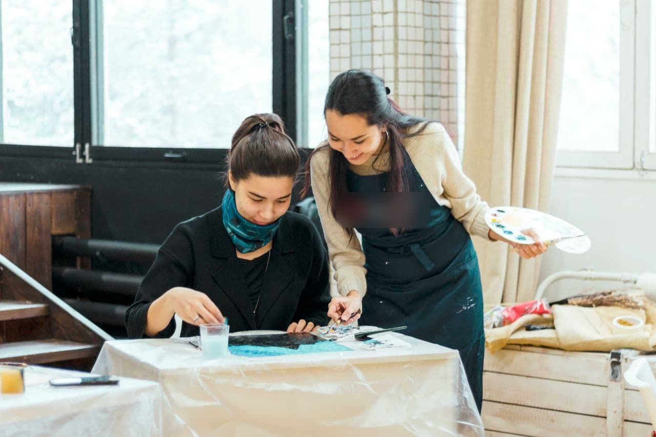 Aliya leaning over a student's painting and guiding her with a brush