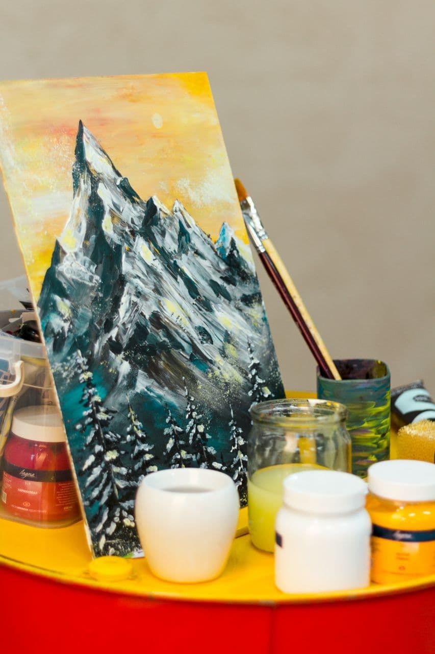 A snowy mountain painting with jars of paint and brushes