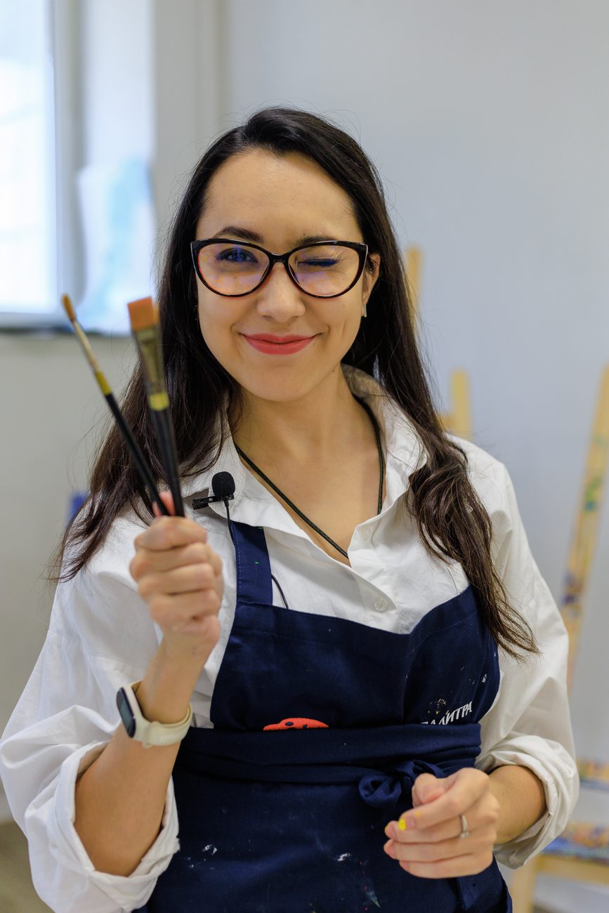 Aliya smiling and winking, holding up two paintbrushes