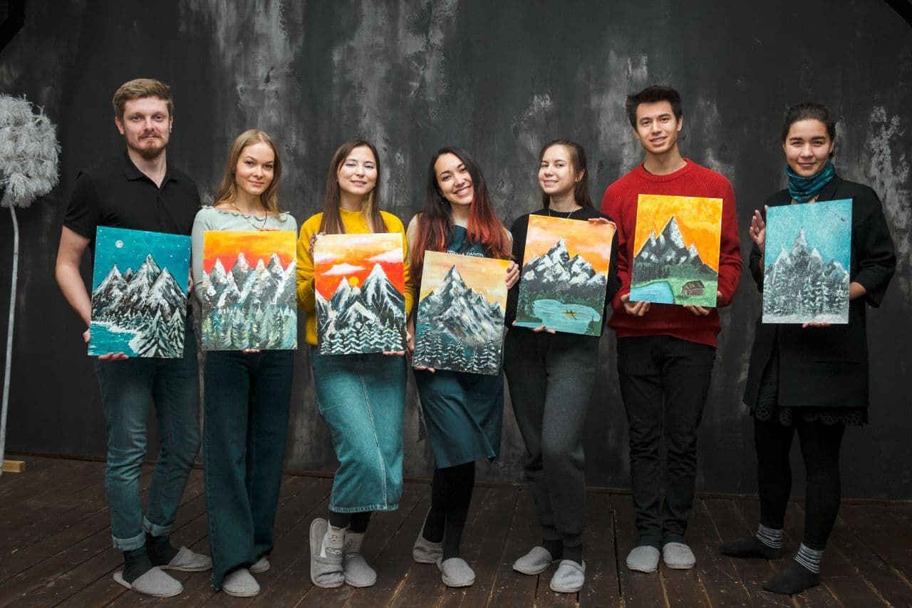 Seven workshop students standing in a row, each holding a mountain painting