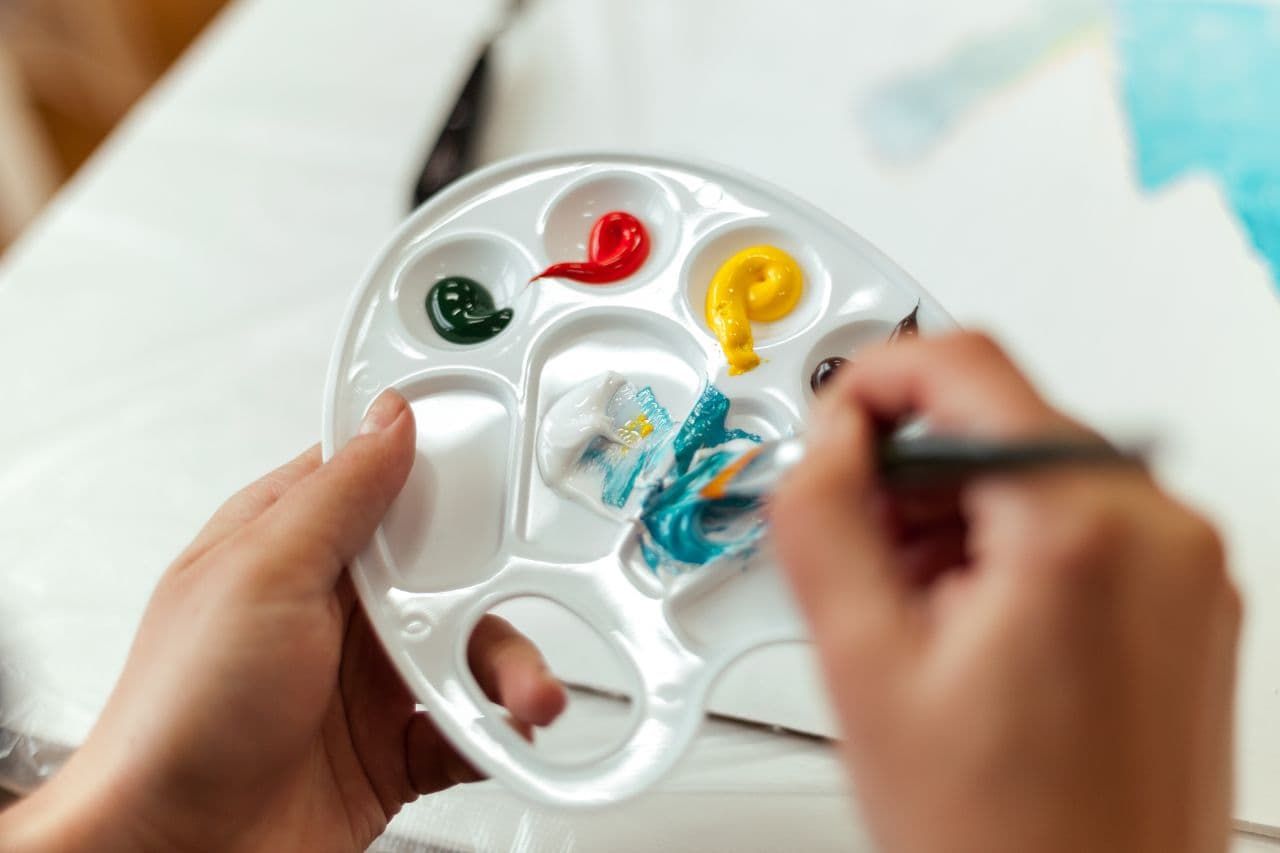 Close-up of hands mixing turquoise paint on a white palette