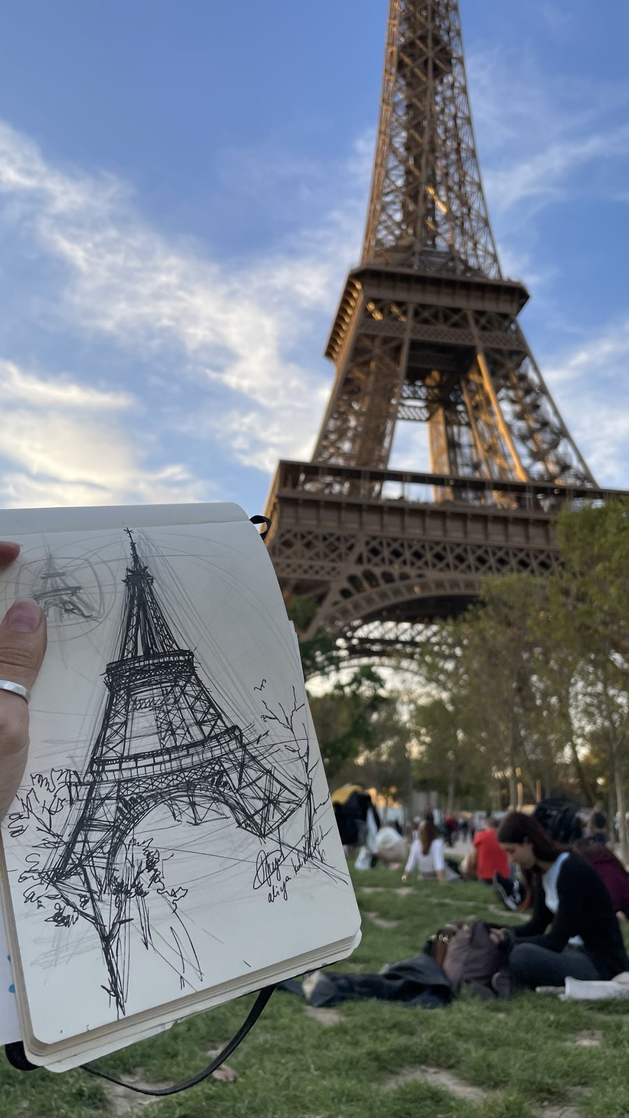 Aliya's ink sketch of the Eiffel Tower held up in front of the tower
