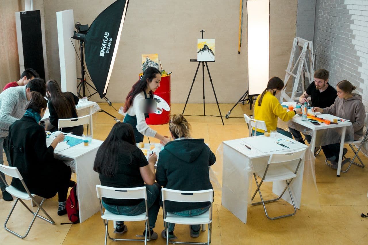 A painting class seen from above, Aliya demonstrating at the easel
